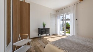 Une chambre à coucher comprenant un lit, une armoire en bois, une petite table de chevet noire avec une plante, et une porte-fenêtre coulissante donnant sur un balcon.