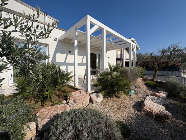 Una casa moderna con un porche cubierto, rodeada de diversas plantas y rocas.