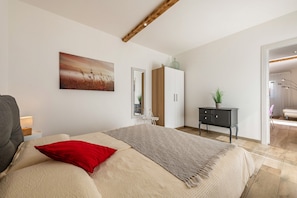 Une chambre à coucher comprenant un lit, une table de chevet, une commode, un miroir et une porte donnant sur une autre pièce.
