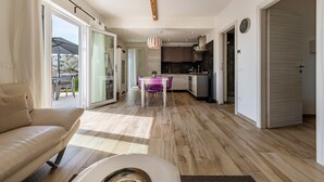 Une cuisine moderne avec des poutres en bois, un coin repas avec des chaises violettes et un canapé dans un salon lumineux.