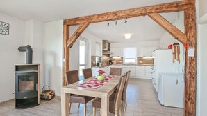 A modern kitchen with white cabinets, a wooden beam ceiling, and a dining area with a table and chairs. - Ferienhaus Grünow OT Ollendorf (Grünow OT Ollendorf)