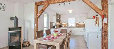 Una cocina moderna con armarios blancos, techo de vigas de madera y comedor con mesa y sillas.