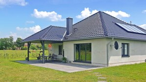 A modern house with a tiled roof, a chimney, and a covered patio with outdoor seating. - Ferienhaus Grünow OT Ollendorf (Grünow OT Ollendorf)