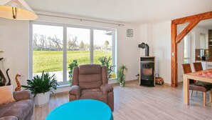 A spacious living room with a large window, a sofa, a table, and a wood-burning stove. - Ferienhaus Grünow OT Ollendorf (Grünow OT Ollendorf)