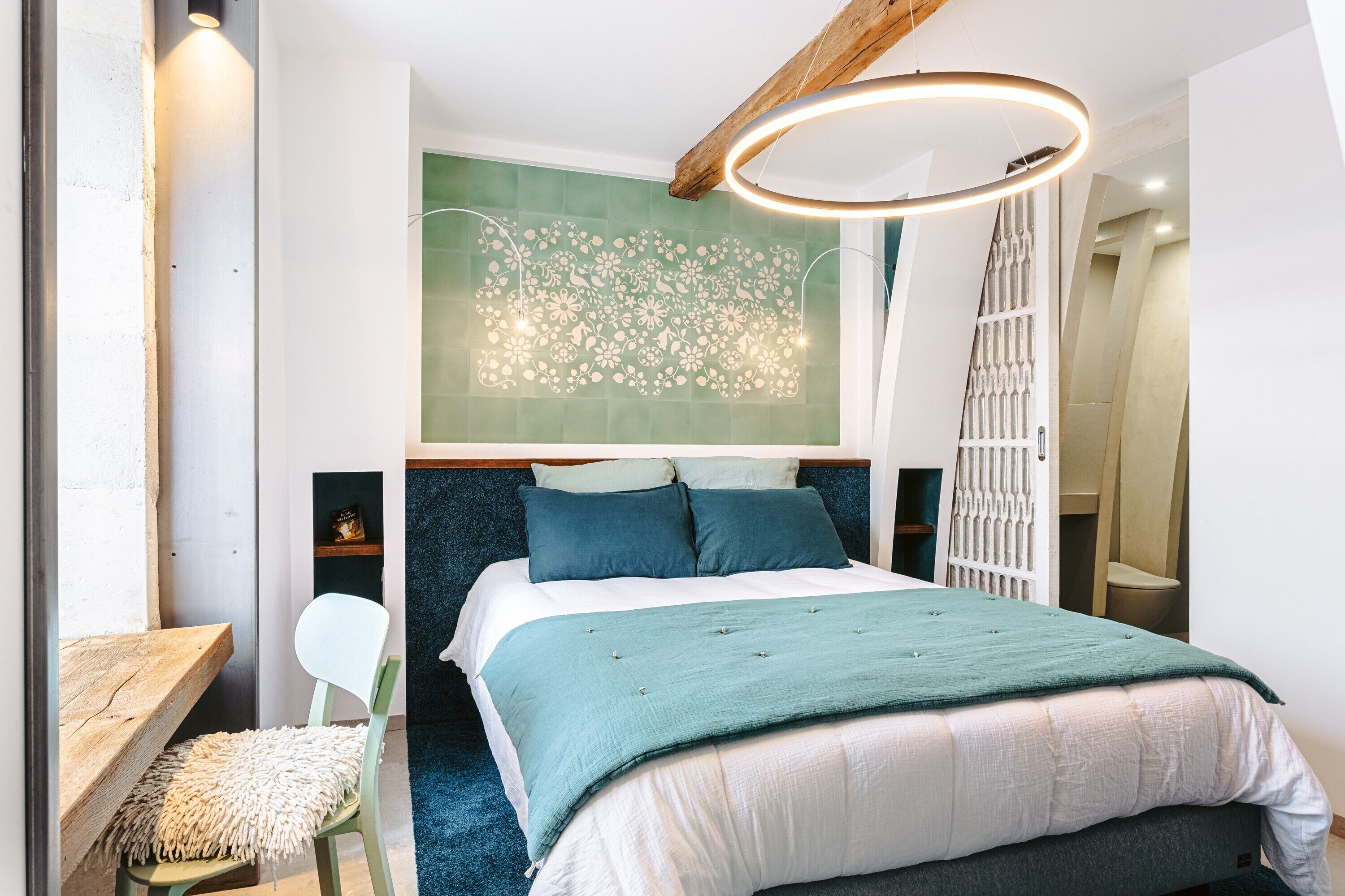 Une chambre à coucher comprenant un lit, une chaise, un bureau et un mur orné d’un motif floral.