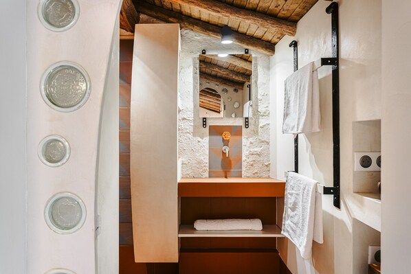 Une salle de bain au décor rustique, avec un plafond en bois, un mur en pierre, une étagère en bois et un porte-serviettes.