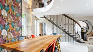 Un interior moderno con una mesa de comedor de madera, sillas coloridas, una escalera y un mural.
