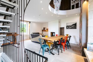 Ein modernes Interieur mit einem Holzesstisch, bunten Stühlen, einer Treppe mit Geländer und einer Kristallleuchter.