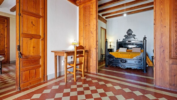 A room with a checkered floor, wooden furniture, a bed with a decorative headboard, and a desk with a chair. - Holiday Home 'Ca Cedó' with Shared Terrace, Wi-Fi and Air Conditioning (La Serra d'Almos)