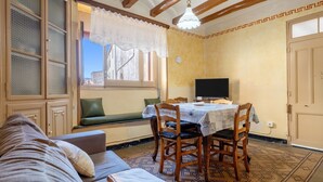 A room with a sofa, a dining table with chairs, a television, a window with a view, and a patterned floor. - Holiday Home 'Ca Cedó' with Shared Terrace, Wi-Fi and Air Conditioning (La Serra d'Almos)