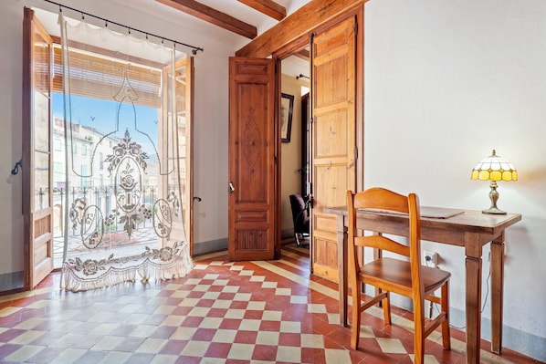 Een kamer met een geruit vloerkleed, een houten bureau met een lamp en een stoel.