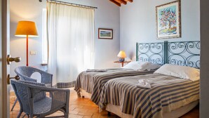A bedroom with two beds, a chair, a lamp, a painting, and a window with curtains. - Apartment 'Casa Rose' with Sea View, Wi-Fi and Air Conditioning (Orbetello)