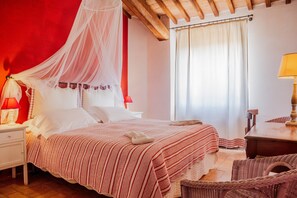 A bedroom with a bed, a nightstand, a wicker chair, a table, and a window with curtains. - Apartment 'Casa Rose' with Sea View, Wi-Fi and Air Conditioning (Orbetello)