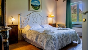 Un dormitorio con una cama, dos lámparas de noche, una silla, un cuadro en la pared y una ventana con cortinas.
