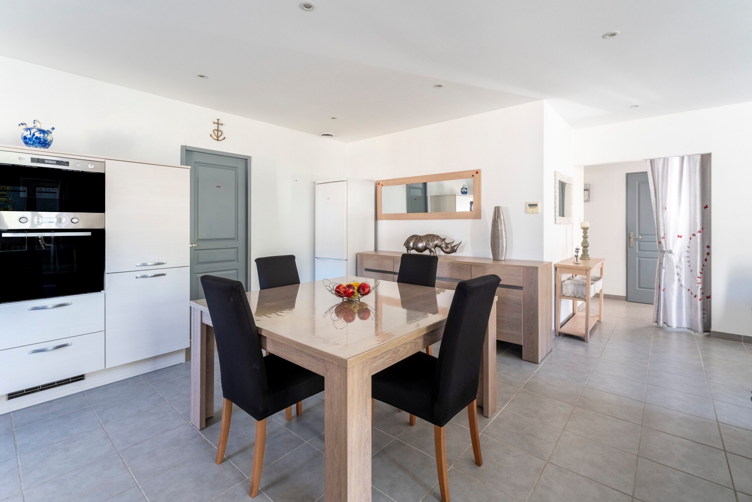 A modern kitchen with a dining area, white cabinetry, and a large mirror.