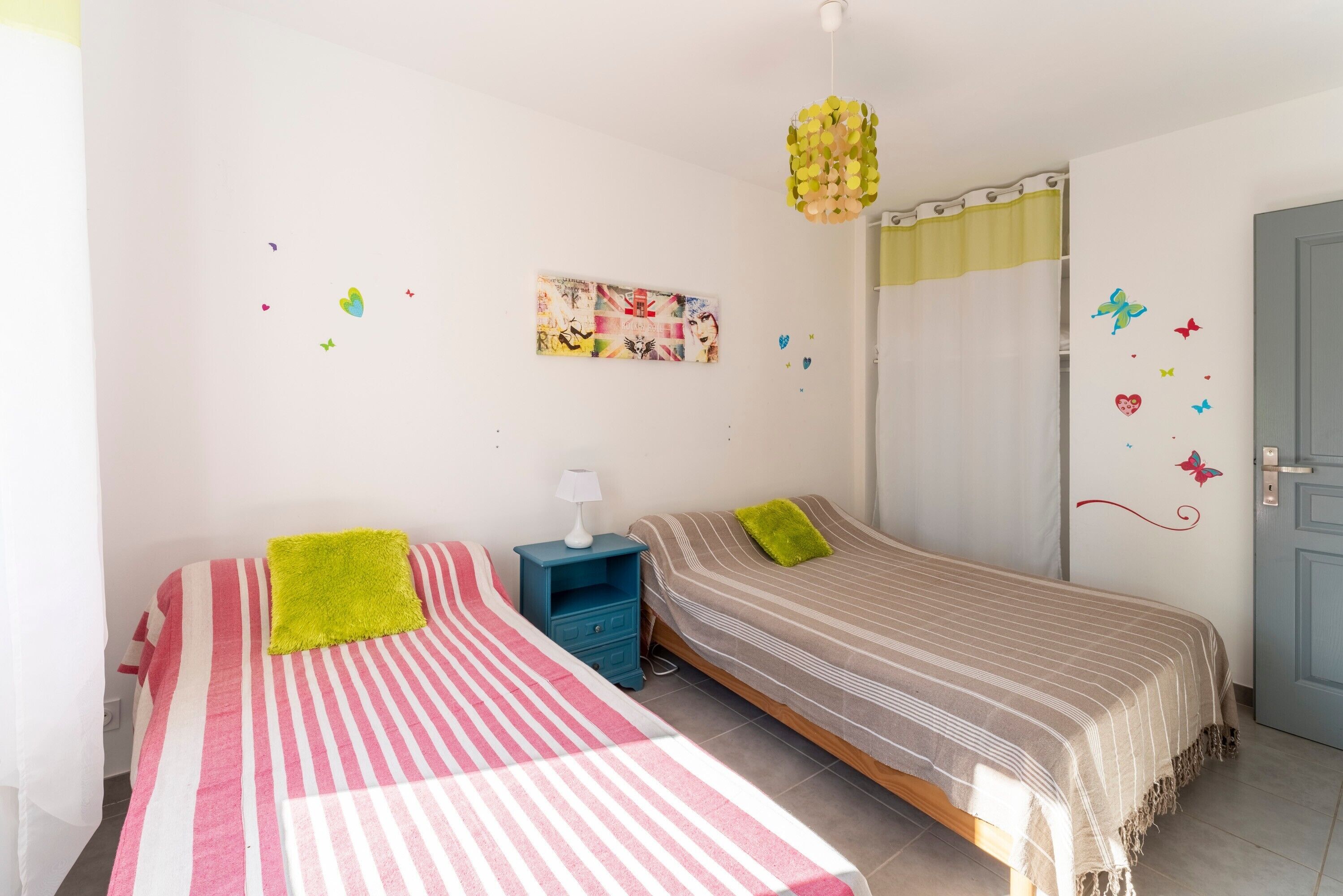 Ein Schlafzimmer mit zwei Betten, einem Nachttisch, einem Wandbild und einer Tür.