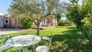 A courtyard with a white metal table and chairs, surrounded by olive trees and a house with a balcony. - Holiday Home “Villa De Maithe” with Private Terrace, Wi-Fi and Air Conditioning (Sernhac)