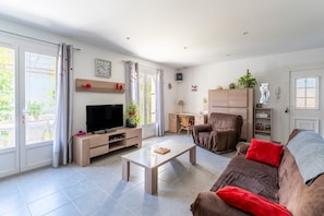 A living room with a TV, coffee table, sofa, and a dining area with a chair and table.