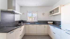 A modern kitchen with a dark countertop, light cabinets, a window with curtains, and a built-in microwave. - Holiday Home “Villa De Maithe” with Private Terrace, Wi-Fi and Air Conditioning (Sernhac)