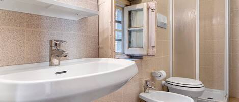A bathroom with a sink, toilet, bidet, and shower.