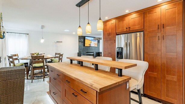 Een moderne keuken met houten kastjes, een roestvrijstalen koelkast, een houten kookeiland en hanglampen.
