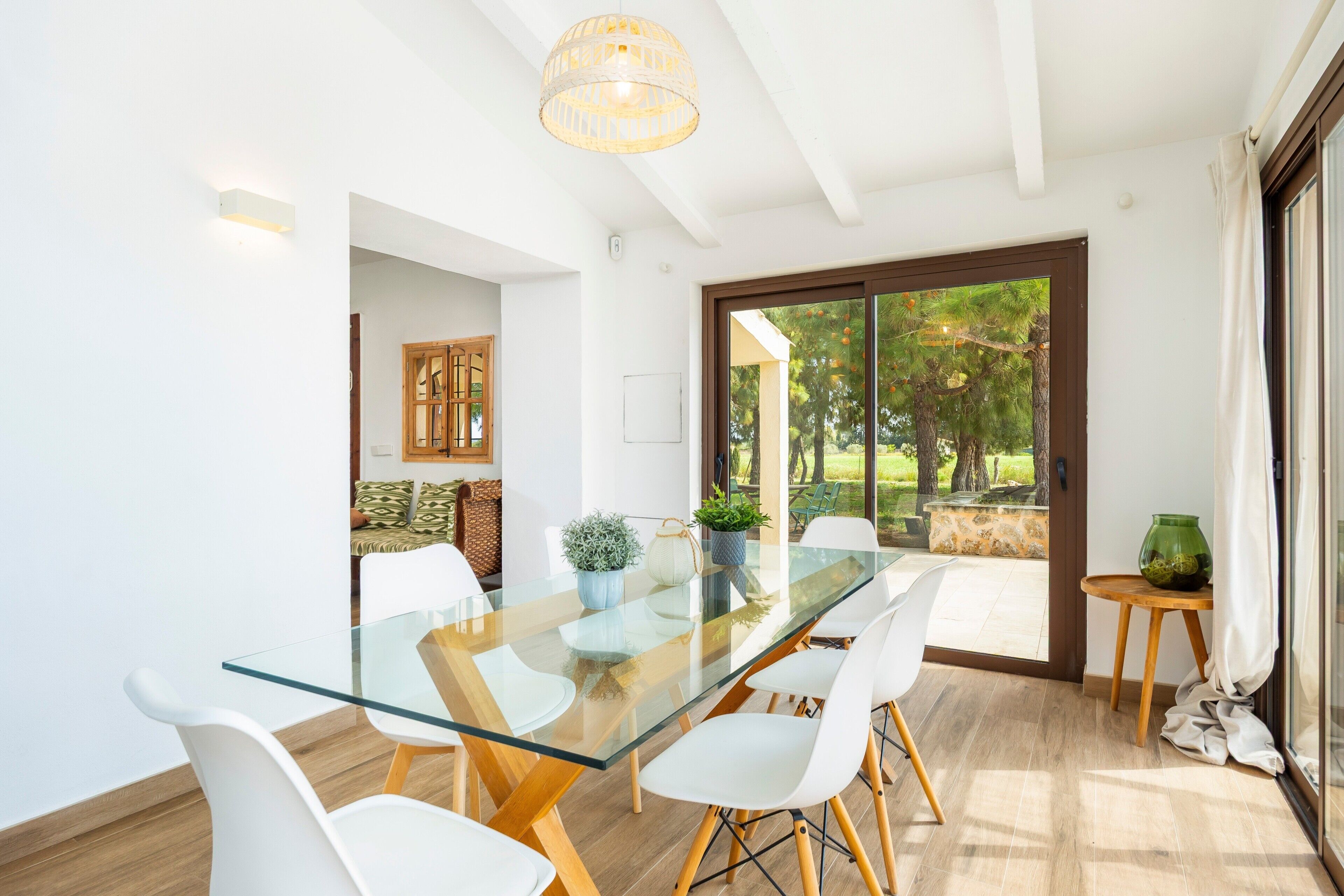 Un espace repas moderne avec une table en verre, des chaises blanches et une vue sur l’extérieur.