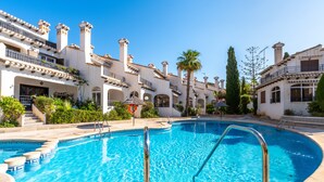 Una piscina con agua cristalina azul, rodeada de edificios con balcones y una palmera.