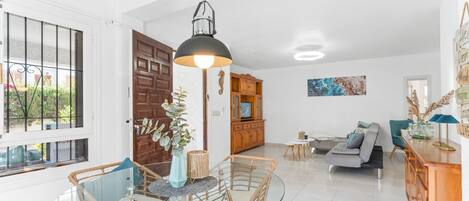 A modern living room with a glass dining table, wicker chairs, a sofa, and a wooden cabinet.