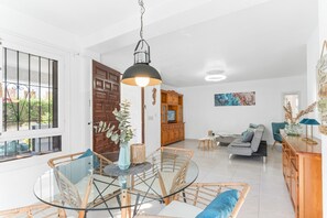 A modern living room with a glass dining table, wicker chairs, a sofa, and a wooden cabinet.