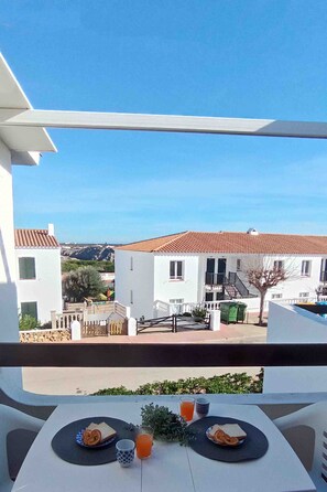 A balcony with a table set for breakfast, overlooking a residential area with white buildings and a clear sky. - Costa Arenal Apartment with Sea View, Premium Pool and Close to the Beach (Arenal d'en Castell)