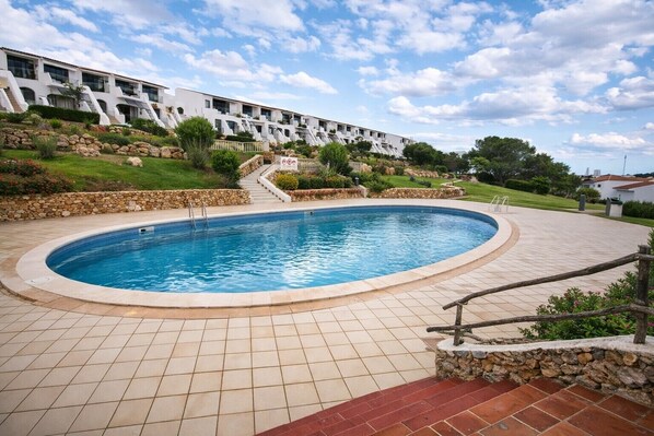 A swimming pool with a stone border, a stone staircase leading to a building, and a clear sky. - Costa Arenal Apartment with Sea View, Premium Pool and Close to the Beach (Arenal d'en Castell)