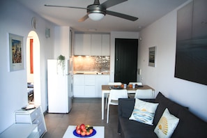 Un espacio habitable compacto con kitchenette, comedor y sofá con almohadones decorativos.
