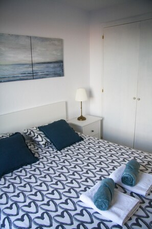 A neatly made bed with heart-patterned bedding, a bedside lamp, and a wardrobe.