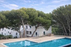 A swimming pool with a white building in the background, surrounded by trees.