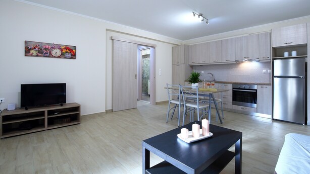 A modern kitchen with stainless steel appliances, a dining area with a table and chairs, and a flat-screen TV on a wooden stand. - Apartment 'Neapolis' with Private Terrace, Wi-Fi and Air Conditioning (?e???da)