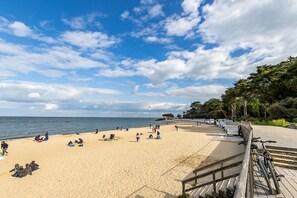 A beach with people sunbathing and walking, a wooden boardwalk, and a sign indicating a marina.