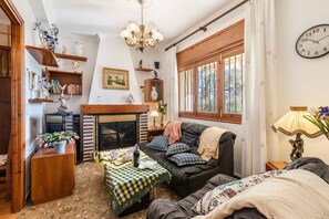 A cozy living room with a fireplace, a sofa, a table with a checkered tablecloth, and a chandelier. - Holiday Home 'Casa Venta Ruizo' with Mountain Views, Wi-Fi and Air Conditioning (Lorca Murcia)