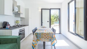 A modern kitchen with a dining table, chairs, and a view through the glass door.