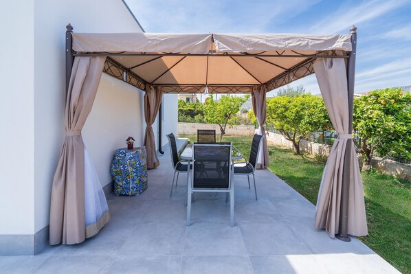 Un espace extérieur abrité, aménagé avec une table et des chaises, un vase décoratif et une nappe à motifs.