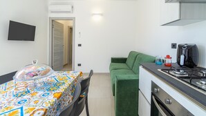 A compact kitchen with a gas stove, a microwave, and a dining area with a table covered by a colorful tablecloth.