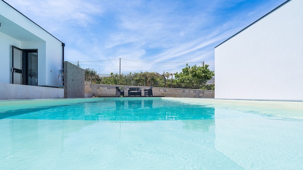 A clear swimming pool with a modern building and a stone wall in the background.