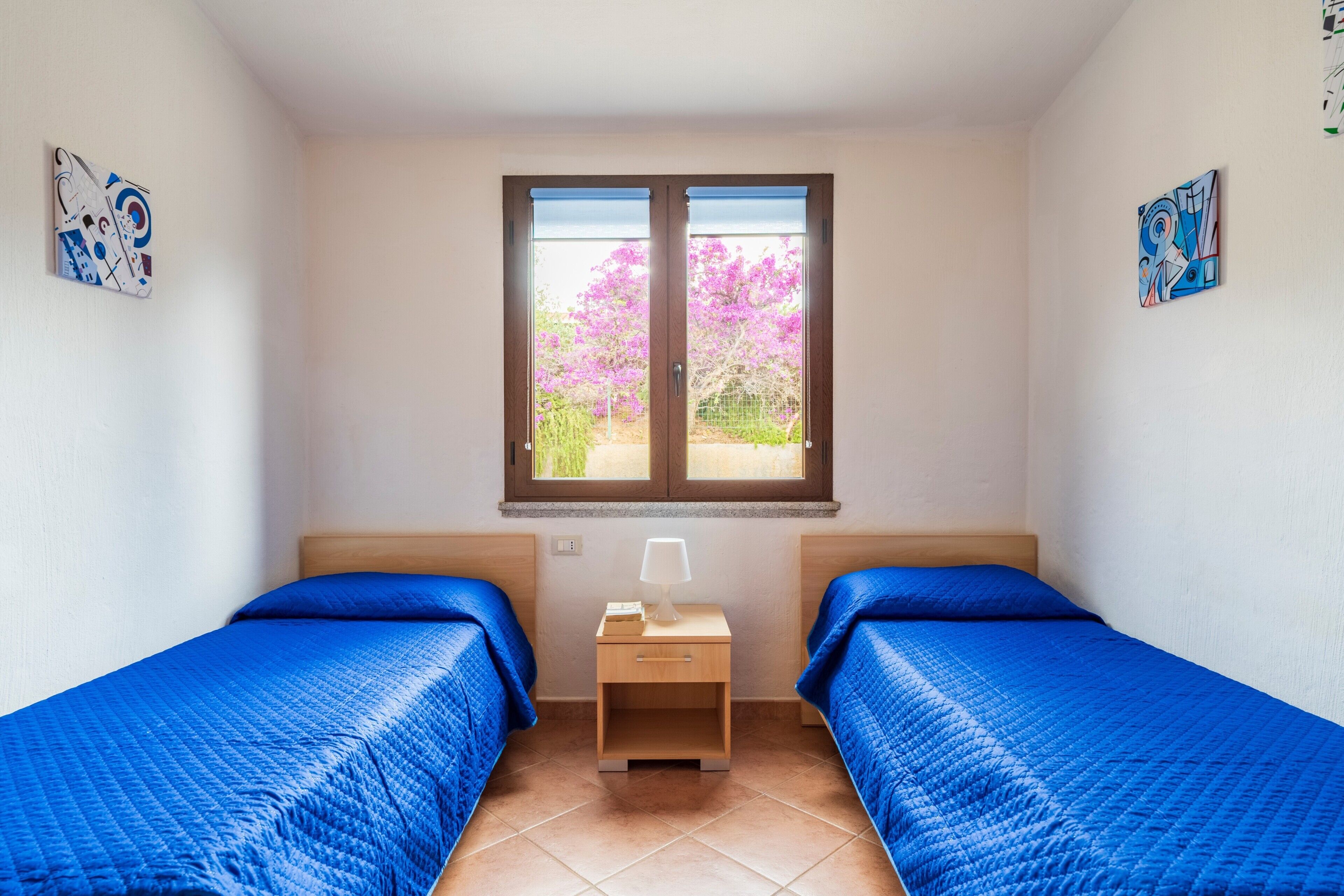 Una habitación con dos camas, una ventana con vistas a flores rosadas y obras de arte en las paredes.