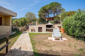 A stone pathway leading to a patio area with a lounge chair and a stone fireplace.