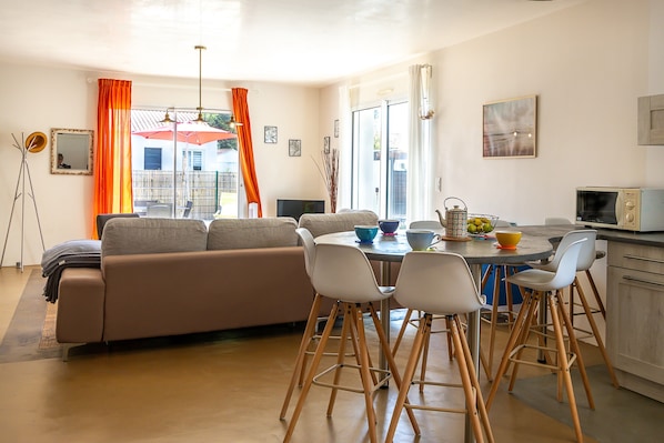 A modern living room with a sofa, dining table, chairs, and a kitchen area with a microwave.