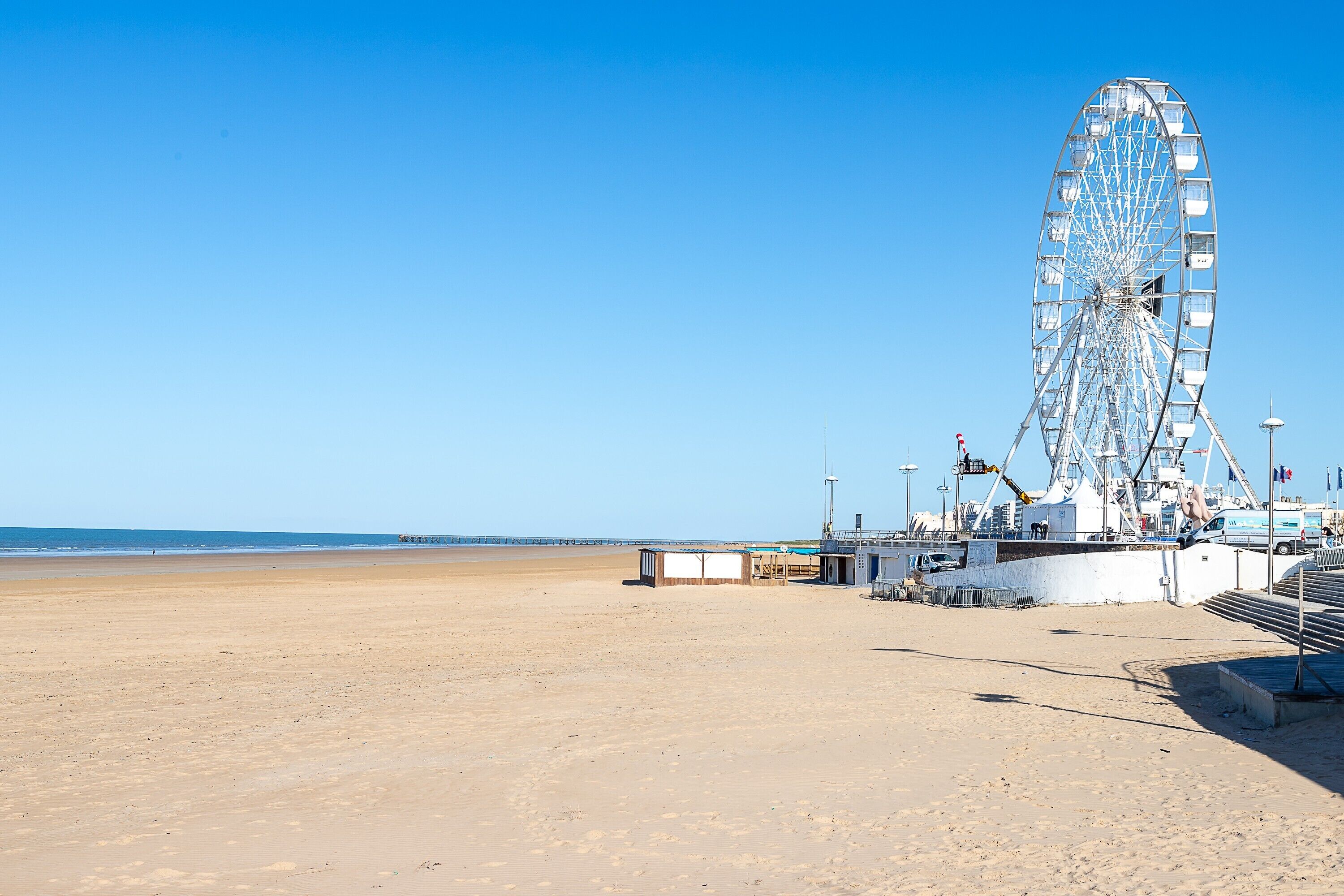Une plage avec une grande grande roue, une jetée et un ciel bleu dégagé.