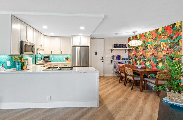 A modern kitchen with white cabinets, a stainless steel refrigerator, and a wooden dining table with chairs.