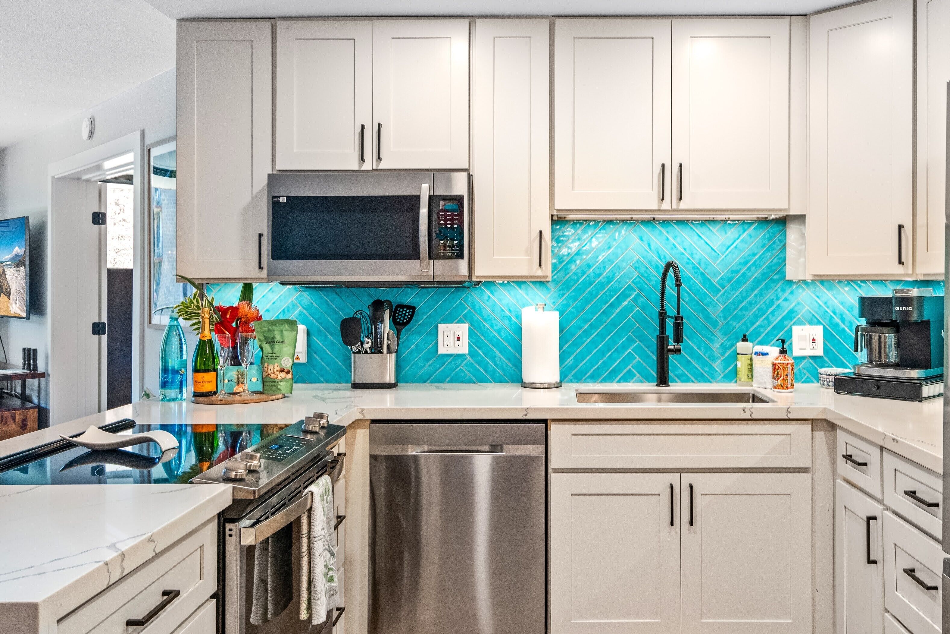A modern kitchen with white cabinets, a stainless steel microwave, and a blue herringbone backsplash.