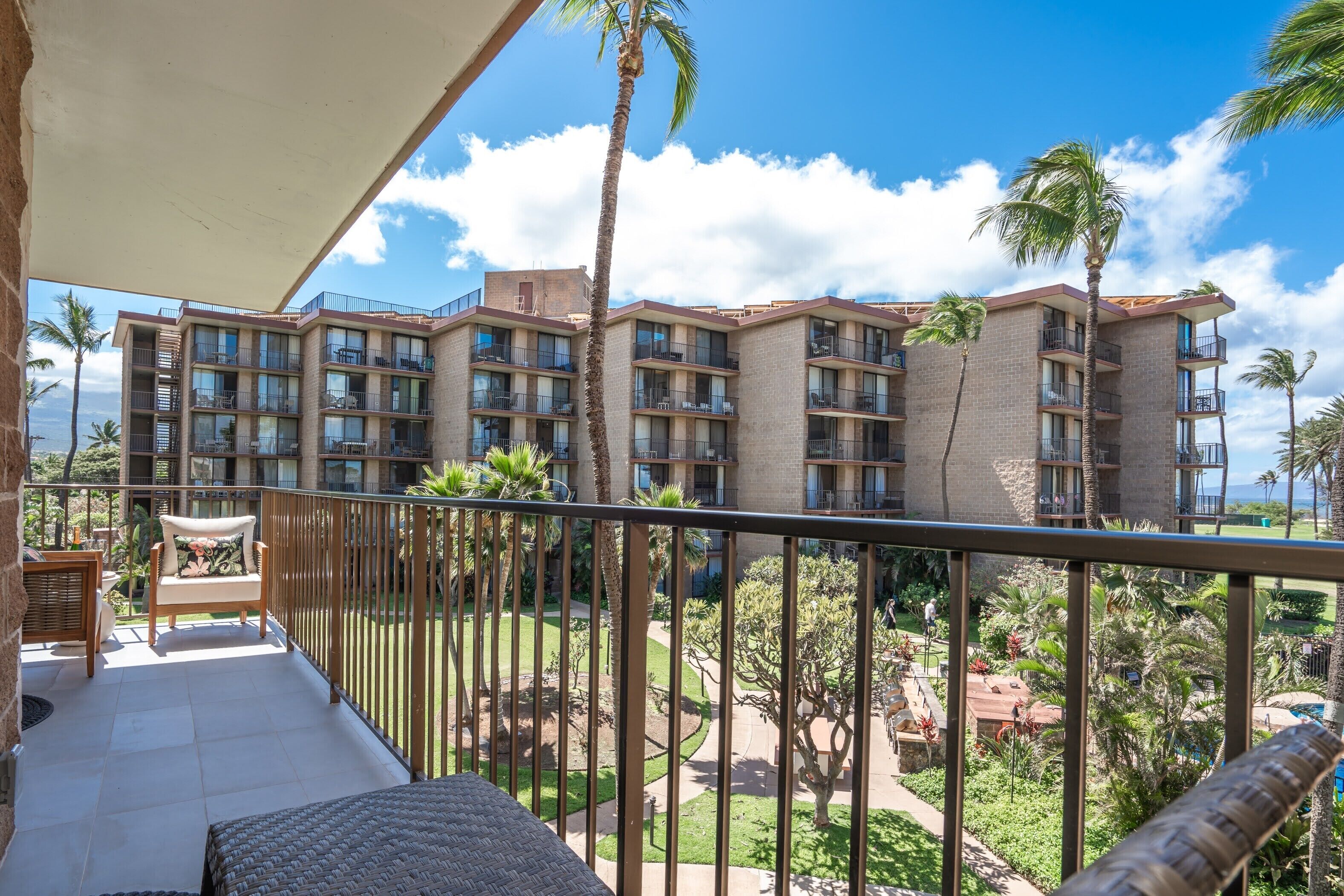 A balcony with a view of a multi-story building, palm trees, and a clear sky.