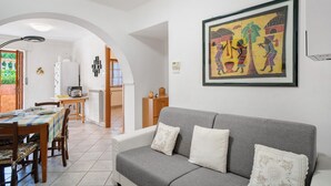 A living room with a grey sofa, a dining table with chairs, a kitchen area, and a framed artwork on the wall. - Apartment 'Casa Di Lo' with Private Terrace and Wi-Fi (Laigueglia)