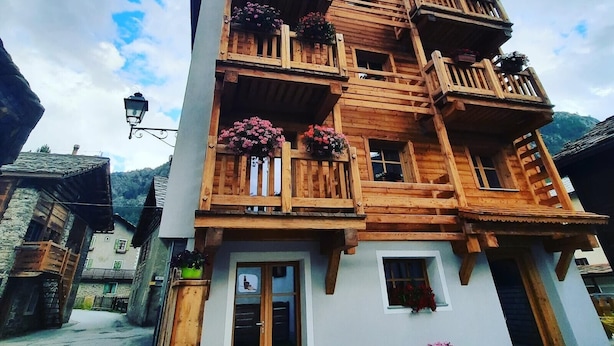 A multi-story wooden building with balconies, a bench outside, and a mountain backdrop.